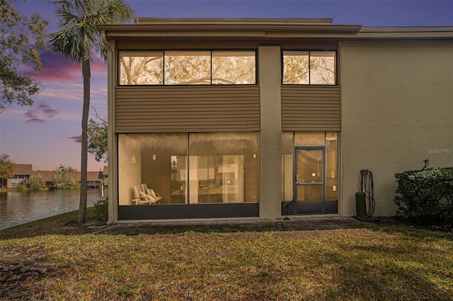 back house at dusk with a lawn and a water view