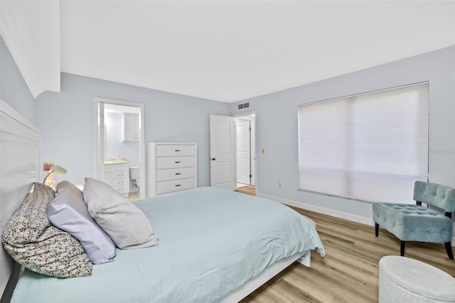 bedroom featuring light wood finished floors, baseboards, visible vents, and connected bathroom