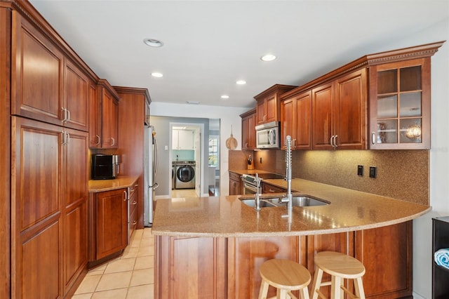 kitchen featuring washer / clothes dryer, stainless steel appliances, a kitchen breakfast bar, kitchen peninsula, and light tile patterned flooring