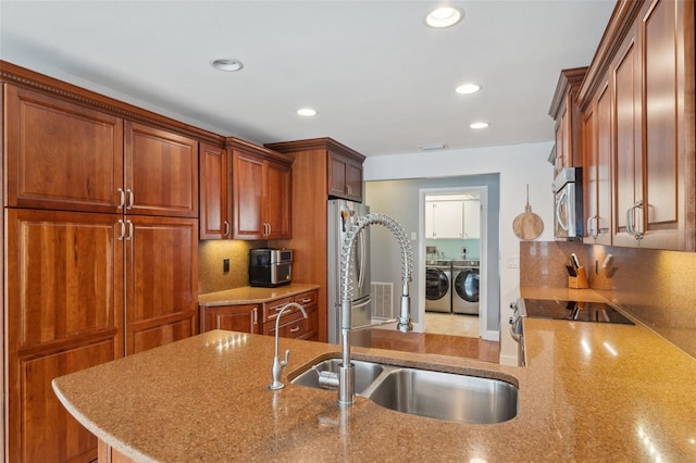 kitchen featuring kitchen peninsula, sink, appliances with stainless steel finishes, separate washer and dryer, and light stone counters