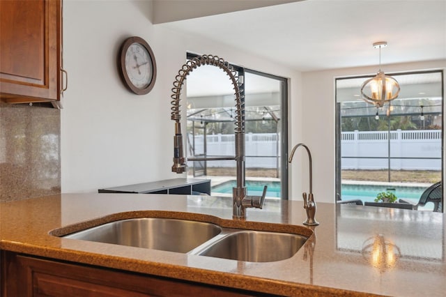 kitchen with light stone countertops, sink, an inviting chandelier, and pendant lighting