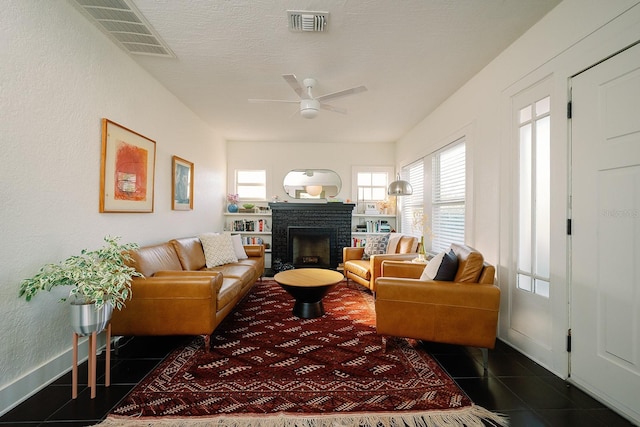 living room featuring a brick fireplace, dark tile patterned floors, and ceiling fan