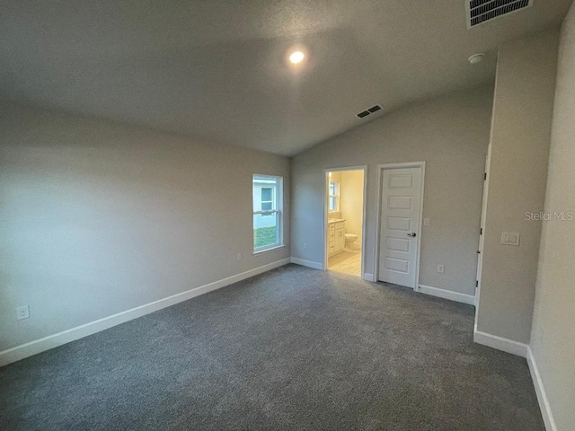 unfurnished bedroom with ensuite bath, lofted ceiling, and dark colored carpet