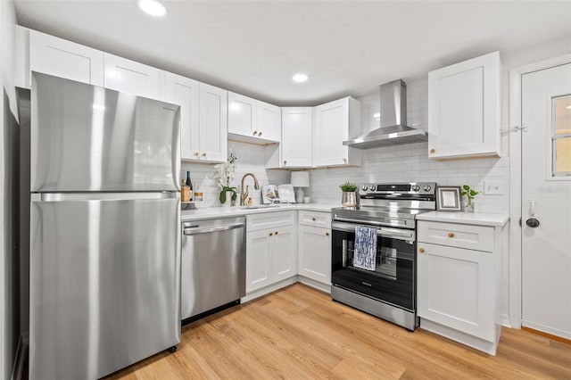 kitchen with wall chimney range hood, sink, white cabinetry, light wood-type flooring, and appliances with stainless steel finishes