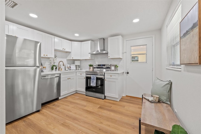 kitchen featuring white cabinets, appliances with stainless steel finishes, wall chimney range hood, decorative backsplash, and light wood-type flooring