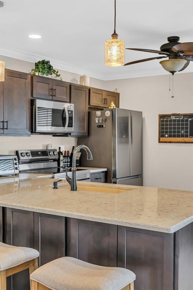 kitchen featuring appliances with stainless steel finishes, hanging light fixtures, ornamental molding, light stone counters, and dark brown cabinets