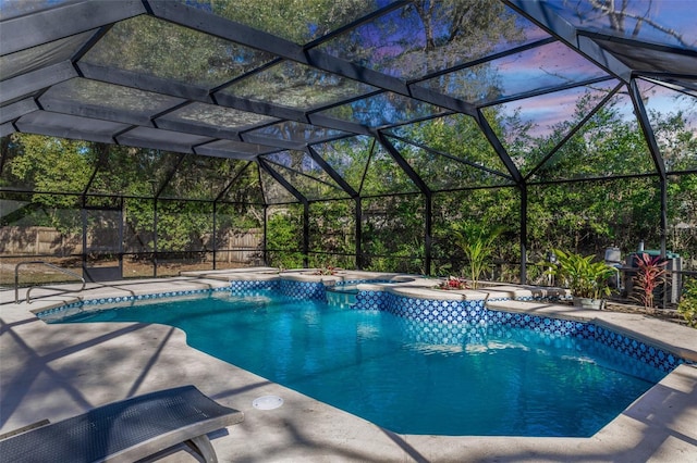 pool at dusk featuring glass enclosure, a patio area, and an in ground hot tub