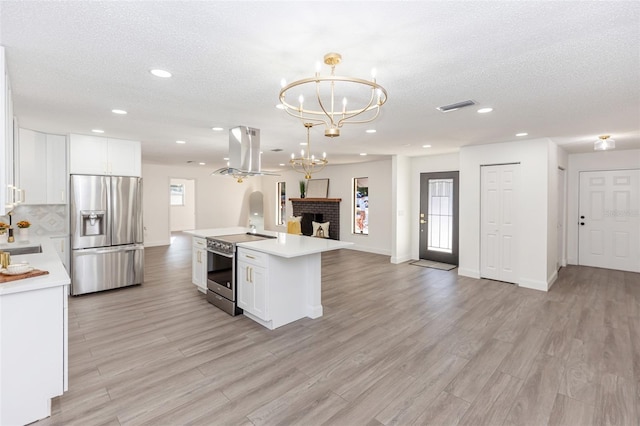 kitchen featuring island exhaust hood, stainless steel appliances, white cabinetry, and hanging light fixtures