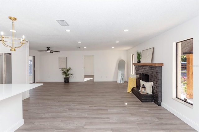 unfurnished living room with light wood-type flooring, ceiling fan with notable chandelier, and a fireplace