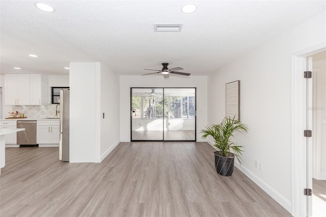 unfurnished living room with ceiling fan, a textured ceiling, and light hardwood / wood-style flooring