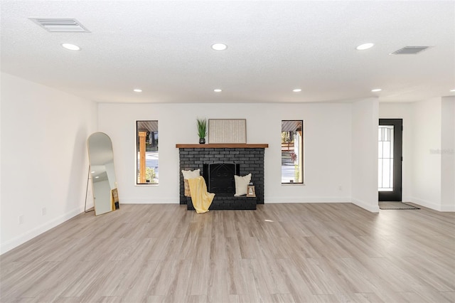 unfurnished room featuring a brick fireplace, light hardwood / wood-style floors, a textured ceiling, and a healthy amount of sunlight