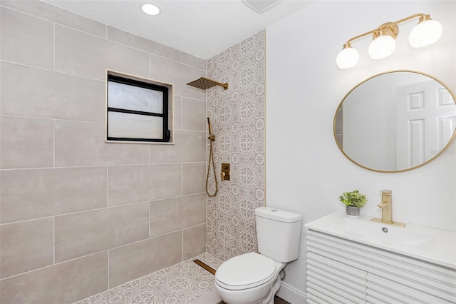 bathroom with a textured ceiling, toilet, vanity, and tiled shower