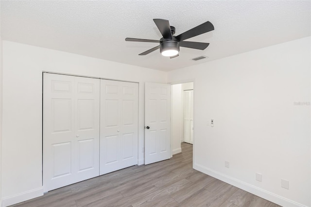 unfurnished bedroom featuring ceiling fan, a closet, light wood-type flooring, and a textured ceiling