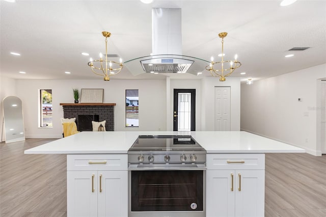 kitchen with electric stove, a brick fireplace, pendant lighting, white cabinetry, and island range hood