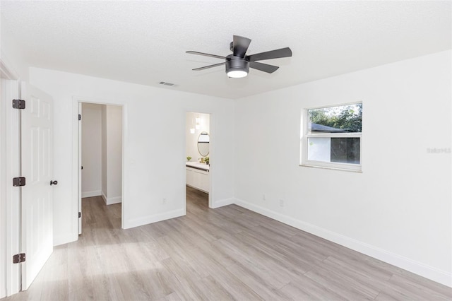 interior space with ceiling fan, connected bathroom, a textured ceiling, a walk in closet, and light hardwood / wood-style flooring