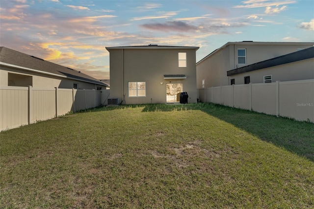 back of house at dusk with central AC unit, a lawn, a fenced backyard, and stucco siding