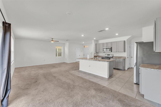 kitchen featuring a center island with sink, gray cabinets, appliances with stainless steel finishes, light tile patterned floors, and light colored carpet