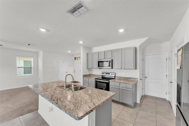 kitchen with visible vents, a center island with sink, gray cabinets, a sink, and appliances with stainless steel finishes