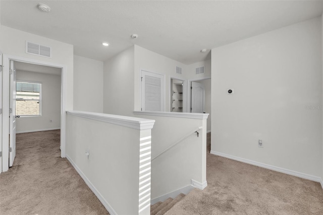 hall featuring baseboards, an upstairs landing, visible vents, and light carpet