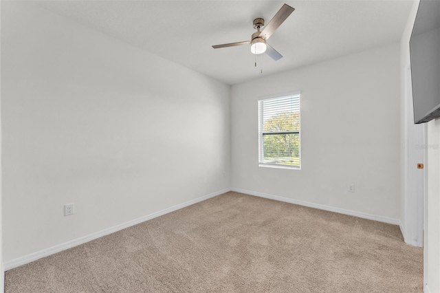 spare room featuring light colored carpet, a ceiling fan, and baseboards