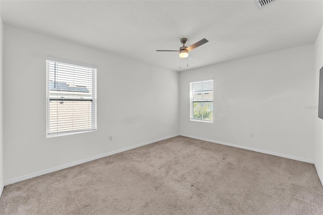 carpeted spare room with visible vents, baseboards, and a ceiling fan