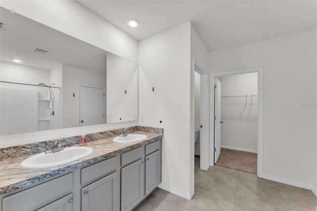 full bath featuring a walk in closet, double vanity, baseboards, and a sink