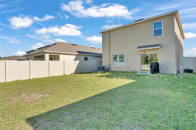 back of property with central air condition unit, stucco siding, a yard, and fence