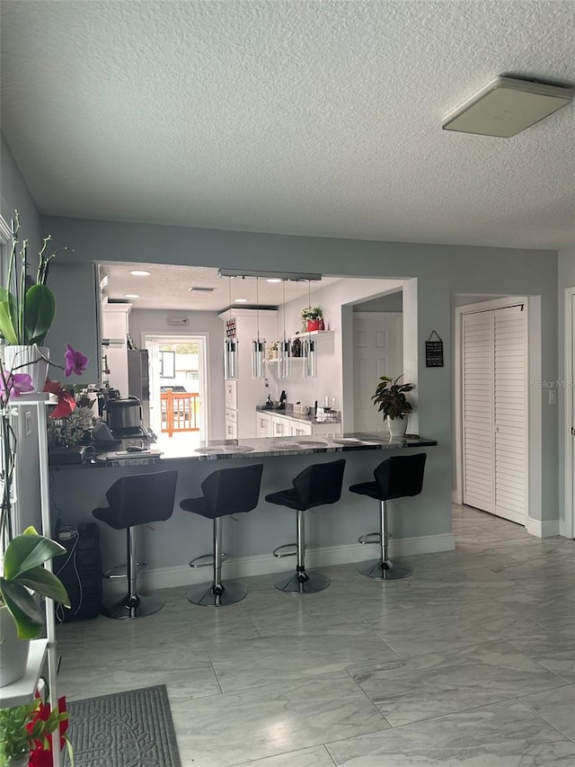 kitchen with decorative light fixtures, a kitchen breakfast bar, kitchen peninsula, and a textured ceiling