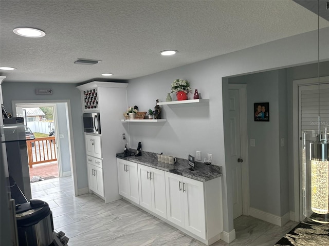 kitchen featuring white cabinets, a textured ceiling, and dark stone counters