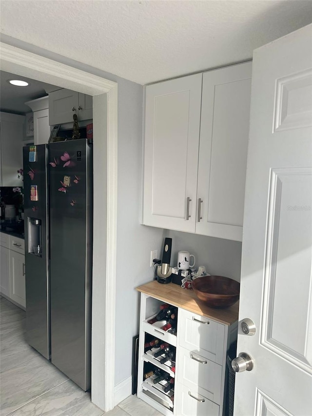 bar featuring wooden counters, white cabinets, a textured ceiling, and stainless steel fridge with ice dispenser