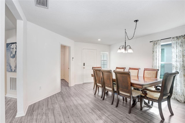 dining room with a textured ceiling, light hardwood / wood-style flooring, a notable chandelier, and a healthy amount of sunlight