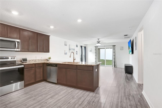 kitchen with kitchen peninsula, sink, light hardwood / wood-style flooring, stainless steel appliances, and light stone counters