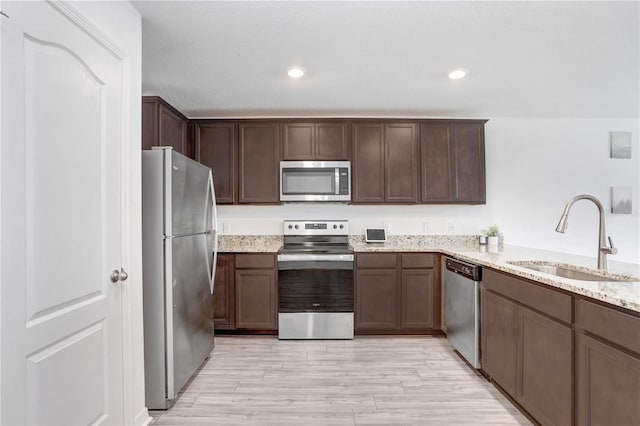 kitchen with light stone countertops, stainless steel appliances, light hardwood / wood-style floors, sink, and kitchen peninsula