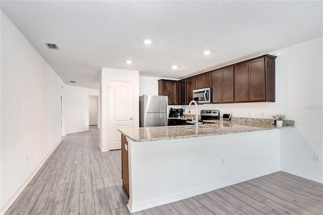 kitchen featuring light hardwood / wood-style floors, kitchen peninsula, stainless steel appliances, light stone counters, and sink