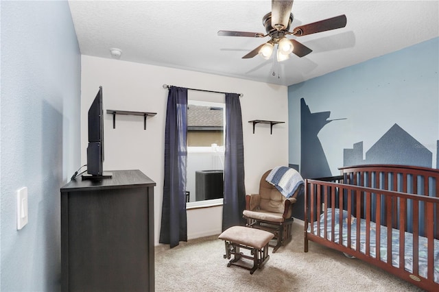 carpeted bedroom with ceiling fan, a nursery area, and a textured ceiling