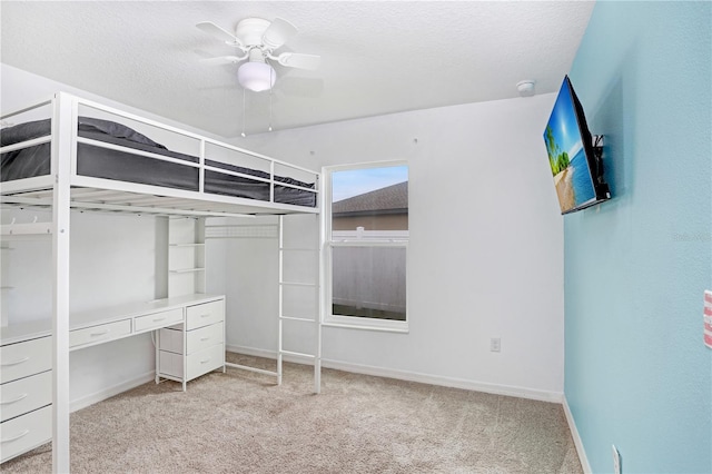 unfurnished bedroom featuring light carpet, a textured ceiling, baseboards, and a ceiling fan