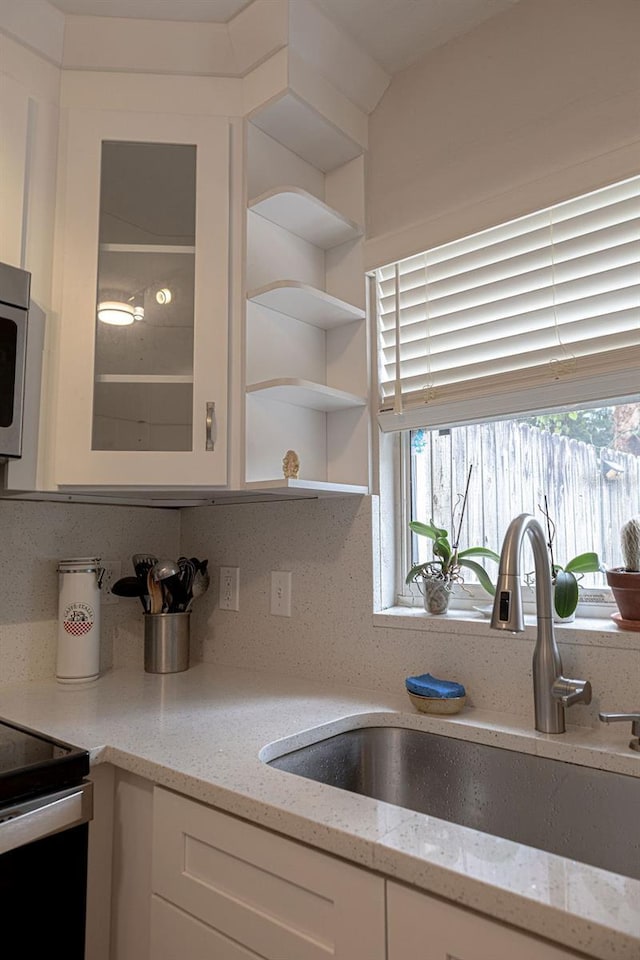 kitchen featuring tasteful backsplash, sink, light stone countertops, and white cabinets