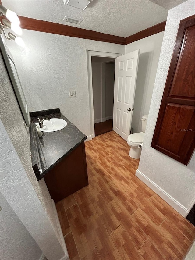 bathroom featuring wood-type flooring, toilet, a textured ceiling, vanity, and ornamental molding