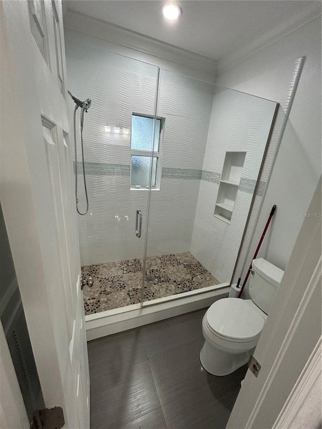 bathroom featuring a shower with door, toilet, and ornamental molding