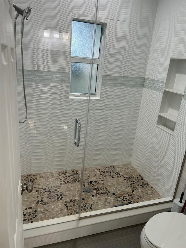 bathroom featuring a shower with shower door and toilet