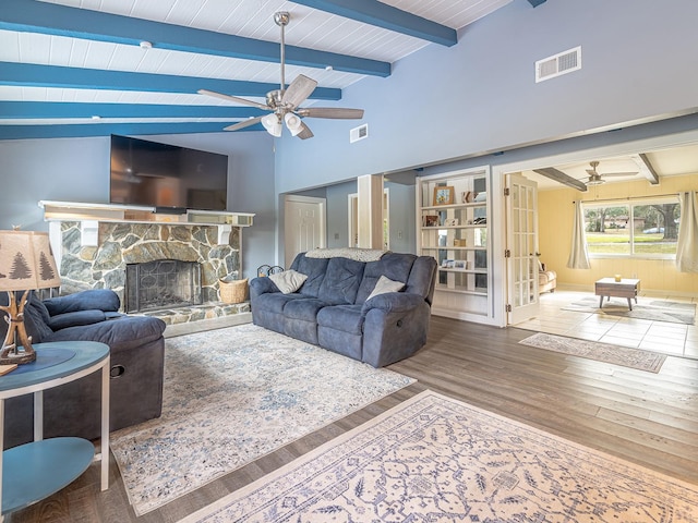 living room featuring wood-type flooring, a stone fireplace, vaulted ceiling with beams, and ceiling fan