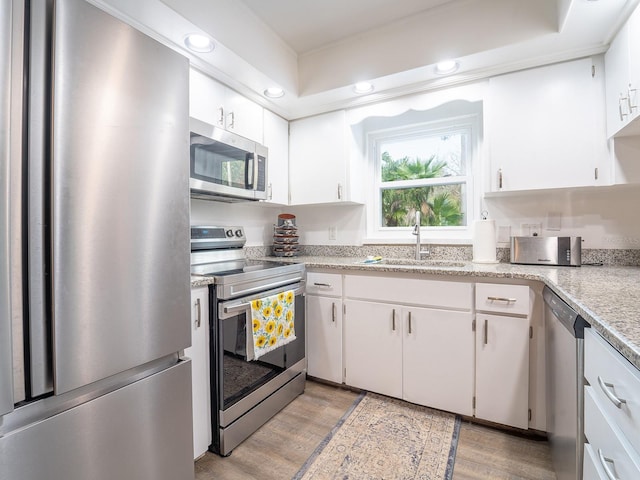 kitchen with white cabinetry, stainless steel appliances, light hardwood / wood-style floors, sink, and a raised ceiling