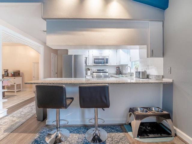 kitchen featuring appliances with stainless steel finishes, white cabinets, sink, light hardwood / wood-style flooring, and a breakfast bar