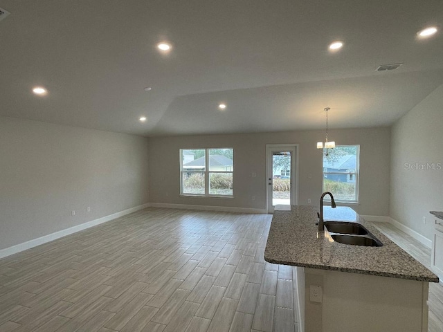 kitchen with a center island with sink, decorative light fixtures, vaulted ceiling, stone counters, and sink