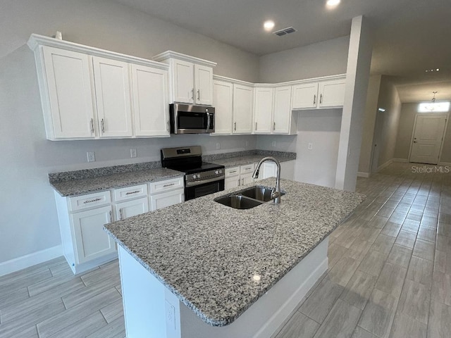 kitchen with appliances with stainless steel finishes, a kitchen island with sink, white cabinets, and sink