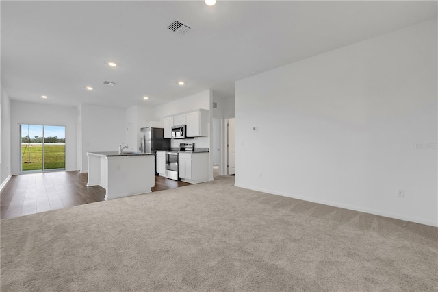 kitchen with dark colored carpet, stainless steel appliances, a kitchen island with sink, white cabinets, and sink