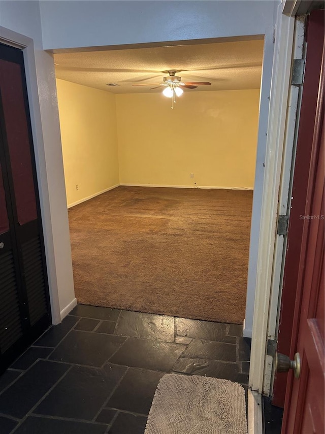 unfurnished room with ceiling fan and dark colored carpet