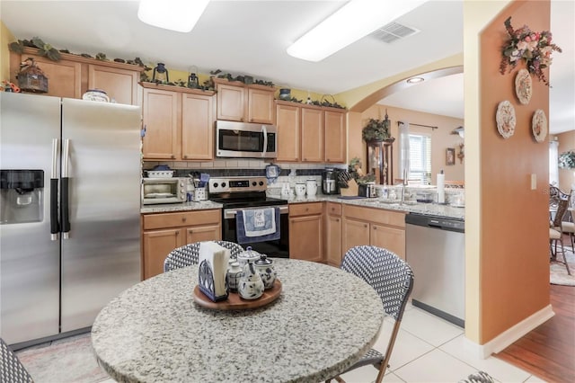 kitchen featuring stainless steel appliances, tasteful backsplash, sink, light stone counters, and light tile patterned floors