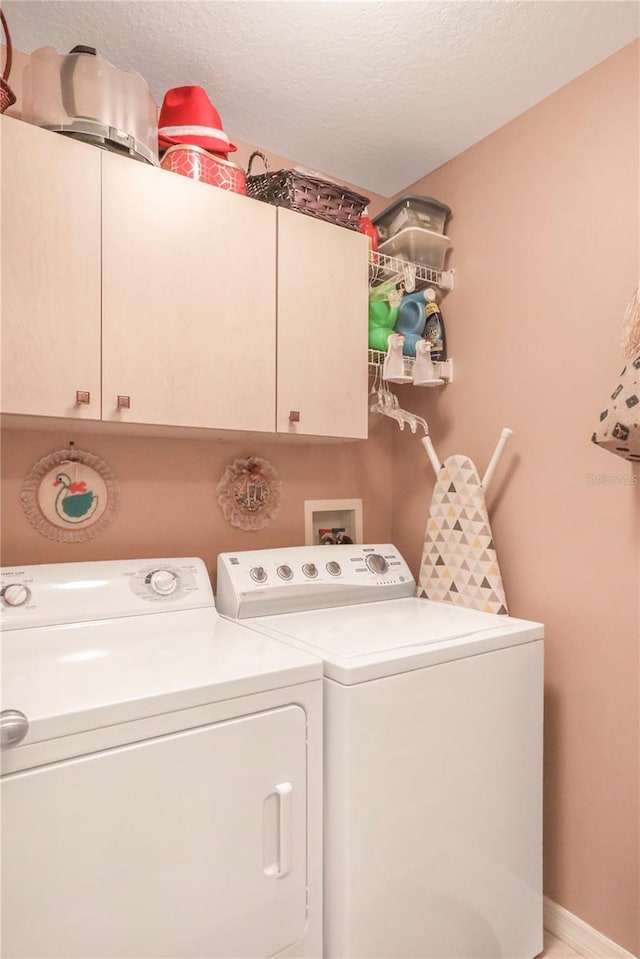 laundry area featuring washer and clothes dryer, a textured ceiling, and cabinets