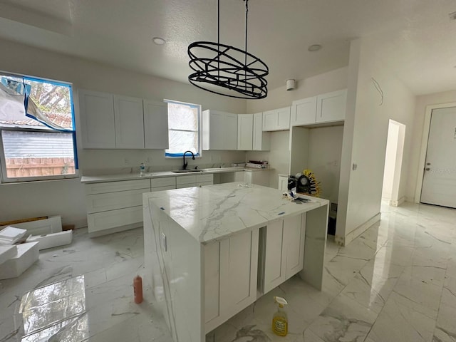 kitchen featuring sink, white cabinetry, a center island, light stone counters, and decorative light fixtures